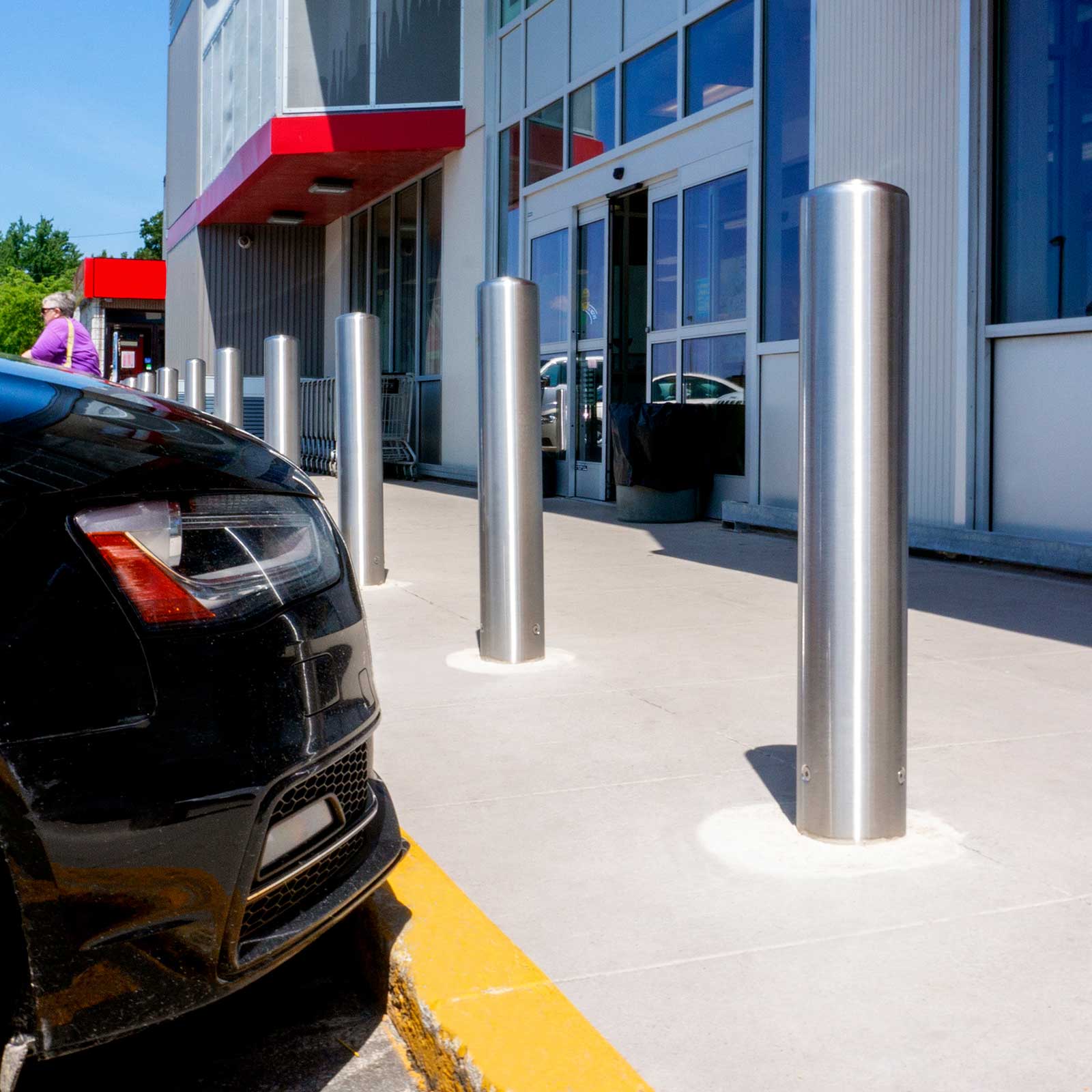 CrashCore Bollard S20 bollards between a nose-in parked car and a storefront entrance.