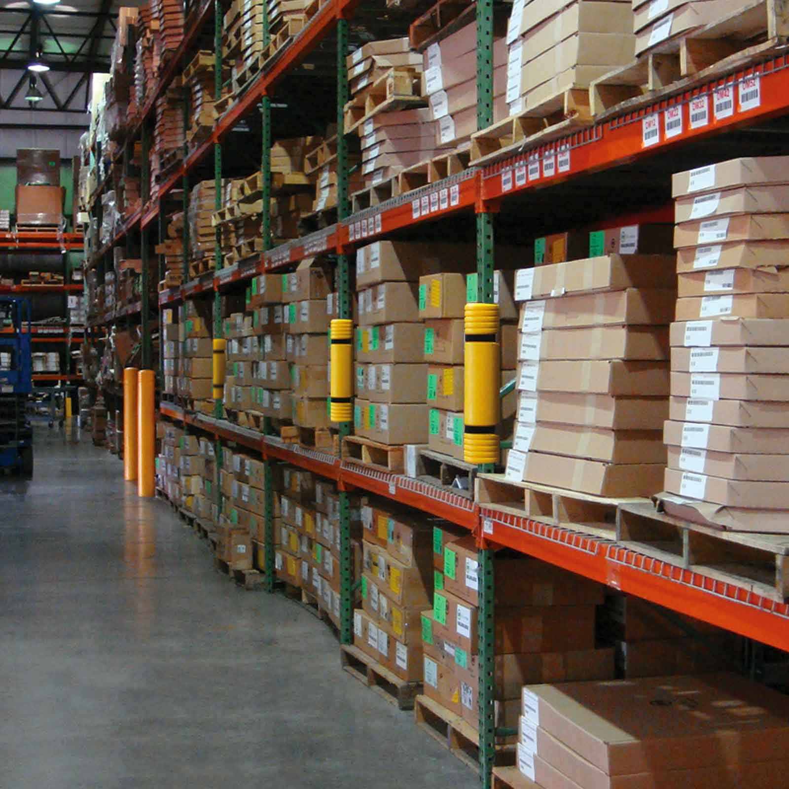 Rack Mounted Guards on green pallet rack uprights with orange beams in an aisle stocked with cartons.