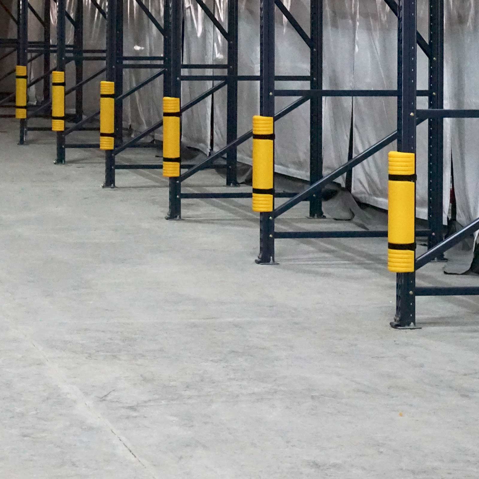 A row of Rack Mounted Guards on dark rack uprights along an empty floor in an industrial facility.